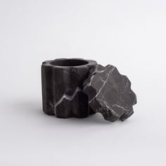 two black rocks sitting next to each other on a white surface with one rock in the middle