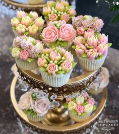 cupcakes decorated with pink and green flowers are on a gold stand in front of other cupcakes