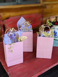 three small pink bags with gold butterflies on them sitting on a table next to flowers