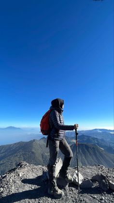 a man with a backpack and skis standing on top of a mountain looking at the sky