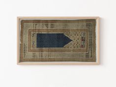 an old rug hanging on the wall with a wooden frame around it that has a blue arrow