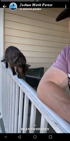 a man standing next to a cat on top of a white balcony railing and looking at the camera