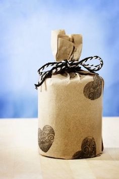 a wrapped gift box with hearts on it and a ribbon tied around the top is sitting on a table