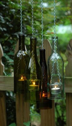 three wine bottles with candles in them hanging from chains