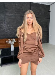 a woman standing in front of a black wall wearing a brown top and short skirt