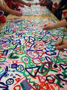 several people are painting letters on a large sheet of paper with colored paint and watercolor pencils