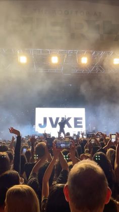 a large group of people at a concert with their hands up in the air and one person taking a photo