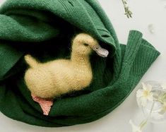 a green scarf with a yellow duck in it and some white flowers on the table