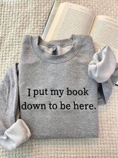 an open book sitting on top of a bed next to a gray sweatshirt with the words i put my book down to be here