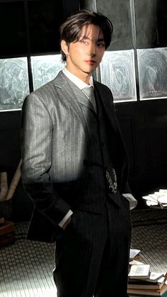 a young man in a suit and tie standing next to stacks of books with his hands on his hips