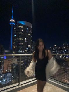 a woman standing on top of a balcony next to a tall building with a city skyline in the background