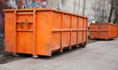 an orange dumpster sitting on the side of a road next to a brick wall