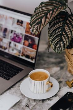 a laptop computer sitting on top of a table next to a coffee cup and phone