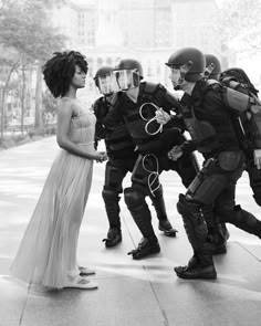 a group of people standing around each other in front of a police officer wearing riot gear