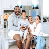 a man and two children are sitting on a kitchen counter with an adult smiling at the camera