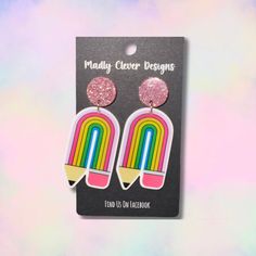 a pair of earrings with pink glitter and rainbows on them, in front of a pastel background