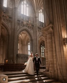 the bride and groom are walking down the stairs in an old cathedral with sunlight streaming through the windows