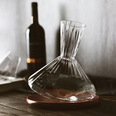 a clear glass vase sitting on top of a wooden table next to a wine bottle