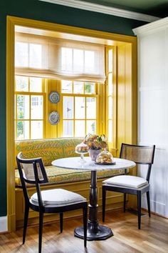 two chairs and a table in front of a window with yellow trim on the windowsill