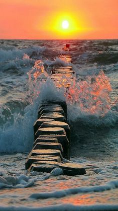 the sun is setting over the ocean with waves coming in from the water and a long pier