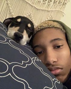 a young man laying on top of a bed next to a black and white dog