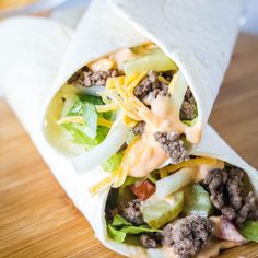 a burrito filled with meat, cheese and lettuce on a cutting board