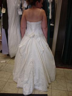 a woman in a white wedding dress looking at herself in the mirror, with her back turned to the camera