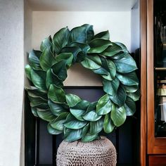 a large green wreath sitting on top of a table next to a vase with leaves