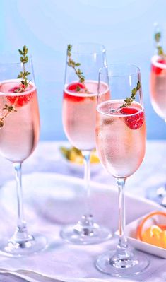 three glasses filled with pink wine and garnished with fresh herbs, sitting on a tray