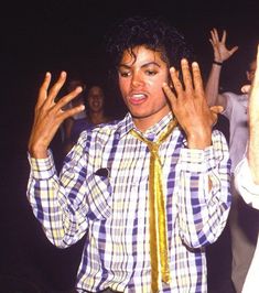 a man in plaid shirt and tie standing next to another man with his hands up