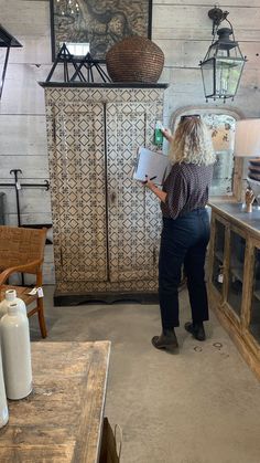 a woman standing in front of a wooden cabinet holding a piece of paper and looking at it