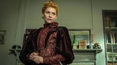 a woman standing in a room with a fireplace and bookshelf behind her, looking at the camera