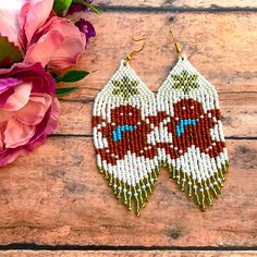 a pair of beaded earrings sitting on top of a wooden table next to flowers