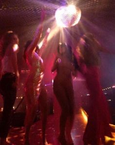 several people dancing at a party with disco balls in the air and lights shining down on them