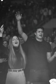 two people standing next to each other in front of a crowd with their hands up