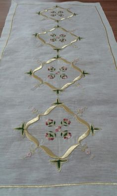 an embroidered table runner with gold trimmings and flowers on white linen, sitting on a wooden floor