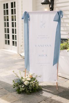 a blue and white wedding sign with flowers on the ground in front of a house