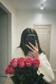 a woman taking a selfie with pink roses in front of her