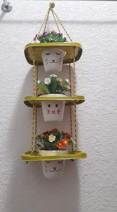 three tiered planters with plants in them hanging on the wall, each holding two cats'heads