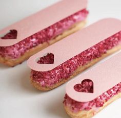 three pink donuts with hearts cut out of them on a white surface, ready to be eaten