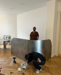 a man standing next to a metal sculpture on top of a hard wood floor