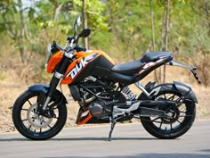 an orange and black motorcycle parked on the side of the road in front of some trees