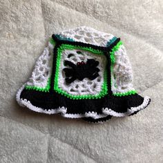 a crocheted black and white dress with green trim on the bottom is laying on a bed