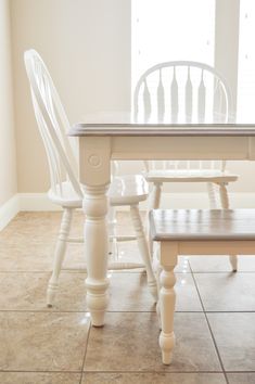 two white chairs and a table in a room with tile flooring, windows and light coming through the window