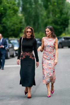 two women walking down the street with one wearing a black dress and another in floral print