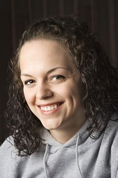 a woman with curly hair smiling at the camera and wearing a gray sweatshirt, black background