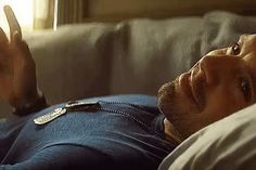 a man laying on top of a white couch next to a window with his hand in the air