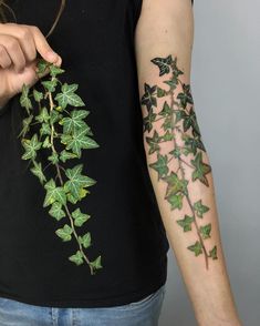 a woman with a tattoo on her arm is holding a green leafy plant and pointing it at the camera