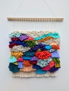 a wall hanging made out of different colored pieces of yarn and thread on a wooden hanger