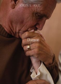 an older man is holding his hand to his face while wearing a gold ring with the word diamond on it